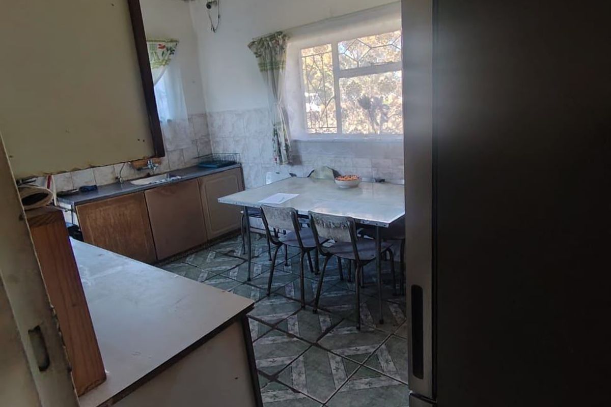A dated kitchen featuring original cabinetry, tiled flooring, and a window with security bars, offering potential for a modern renovation.