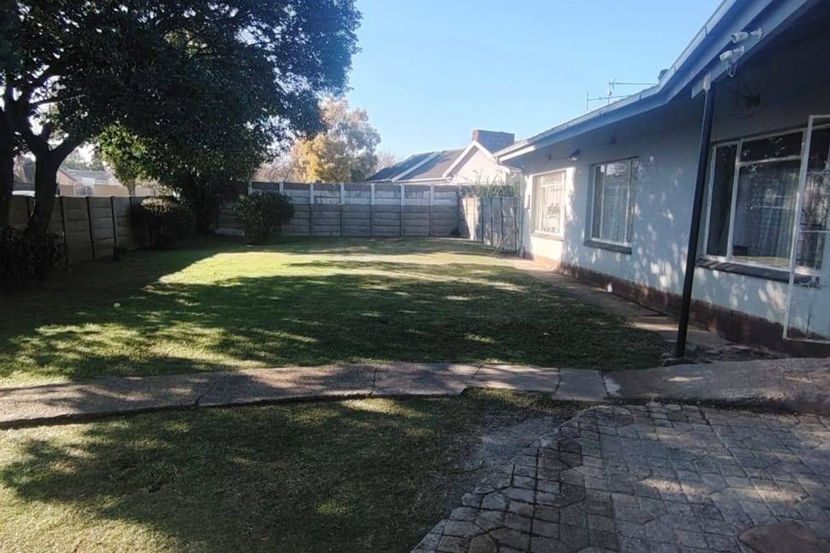 Spacious rear garden featuring a paved patio area, established lawn, and secure boundary walling, offering potential for outdoor landscaping and entertainment space.