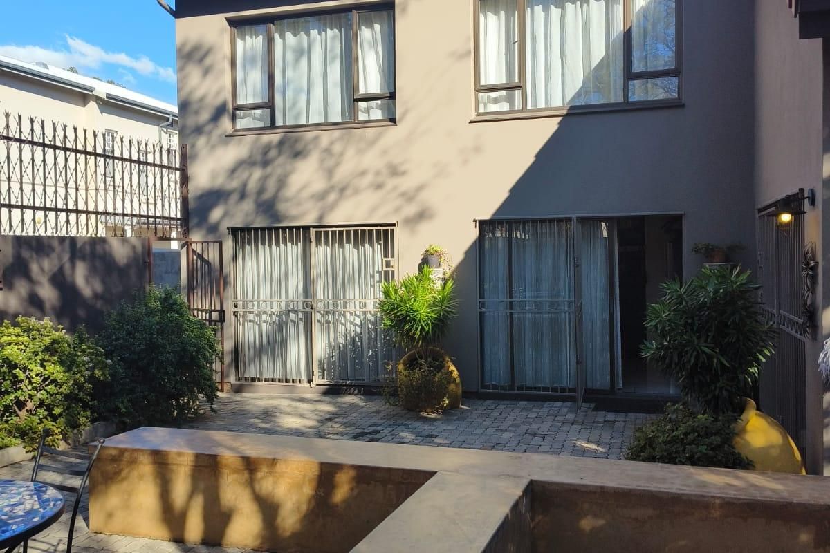 Rear exterior view of a townhouse featuring a paved patio area with a built-in concrete bench, sliding glass doors, and security gates.