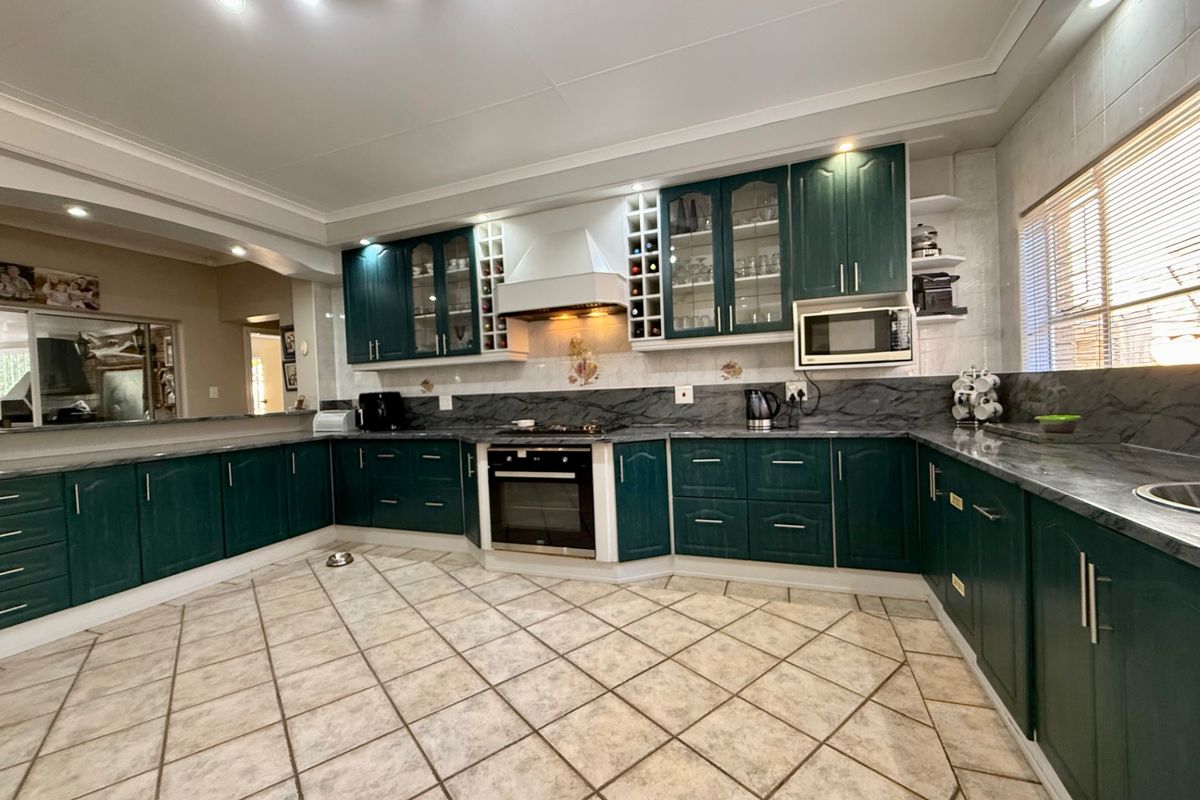 Spacious kitchen featuring dark green cabinetry, stone-look countertops, built-in oven, extractor fan, and tiled flooring with ample storage space.