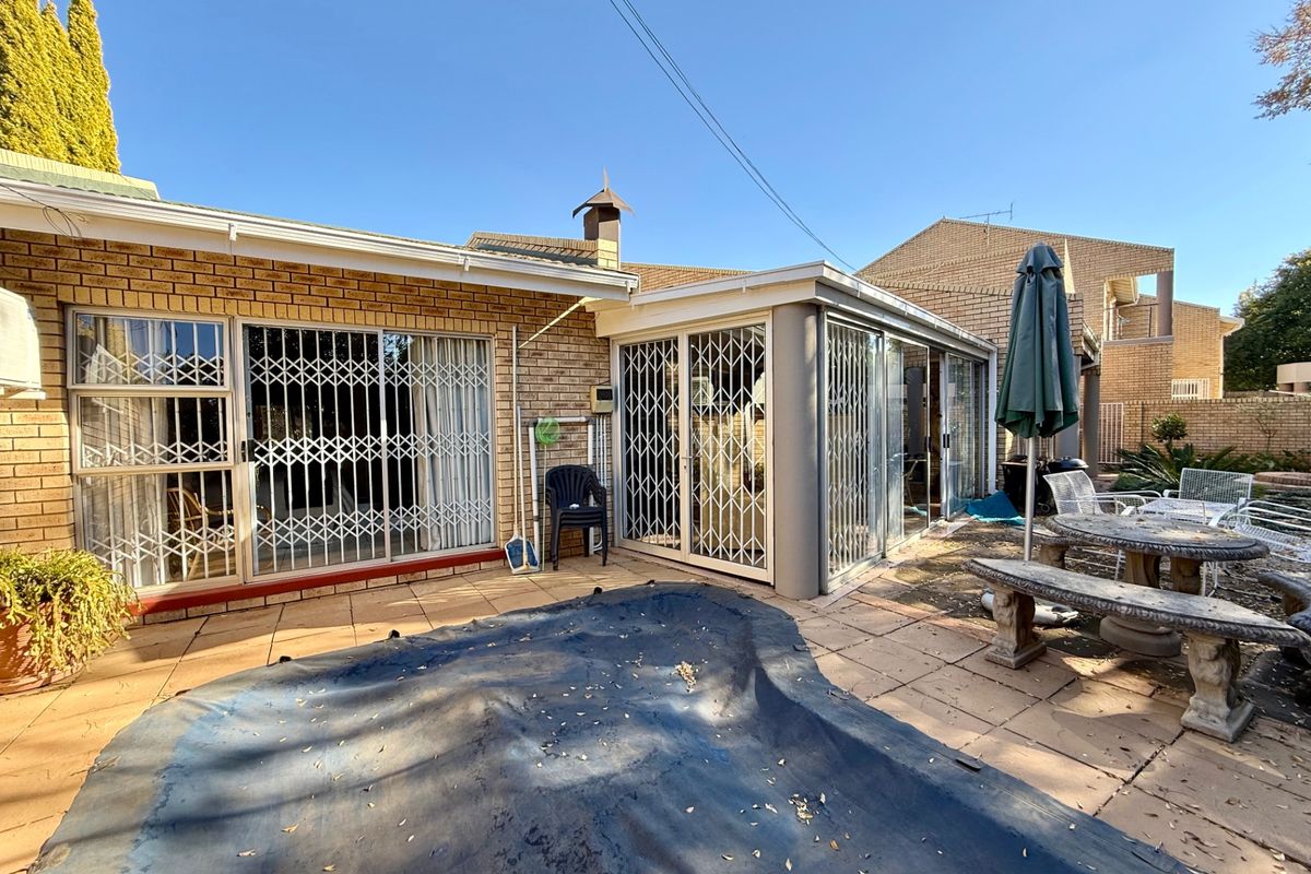 Rear patio area featuring brick facade, sliding glass doors with security gates, and paved outdoor space adjacent to the pool area.