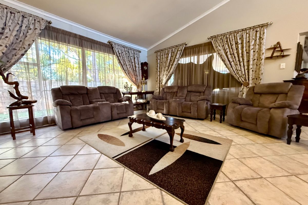Spacious living room featuring large windows with curtain tracks, tiled flooring, and a vaulted ceiling, offering ample natural light.