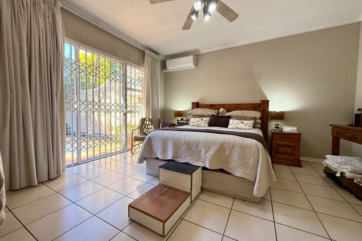 Spacious bedroom featuring tiled flooring, a ceiling fan, and a wall-mounted air conditioning unit, with direct access to the patio through sliding security doors.
