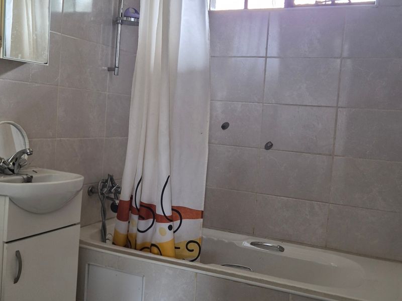 A functional bathroom featuring a bathtub with shower mixer, vanity basin, and tiled finishes. The space requires minor repairs to the wall tiling.