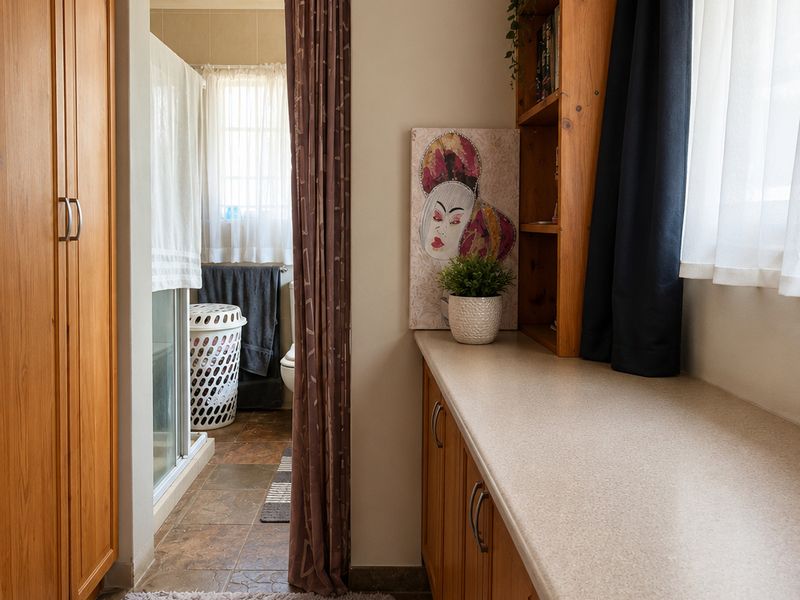A functional laundry area featuring extensive built-in wooden cabinetry, ample counter space, and integrated shelving, leading through to an adjacent bathroom.