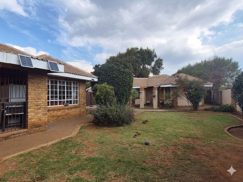 A view of the rear garden featuring face brick exterior walls, tiled roofing, solar panels, and a paved walkway leading to the house entrance.