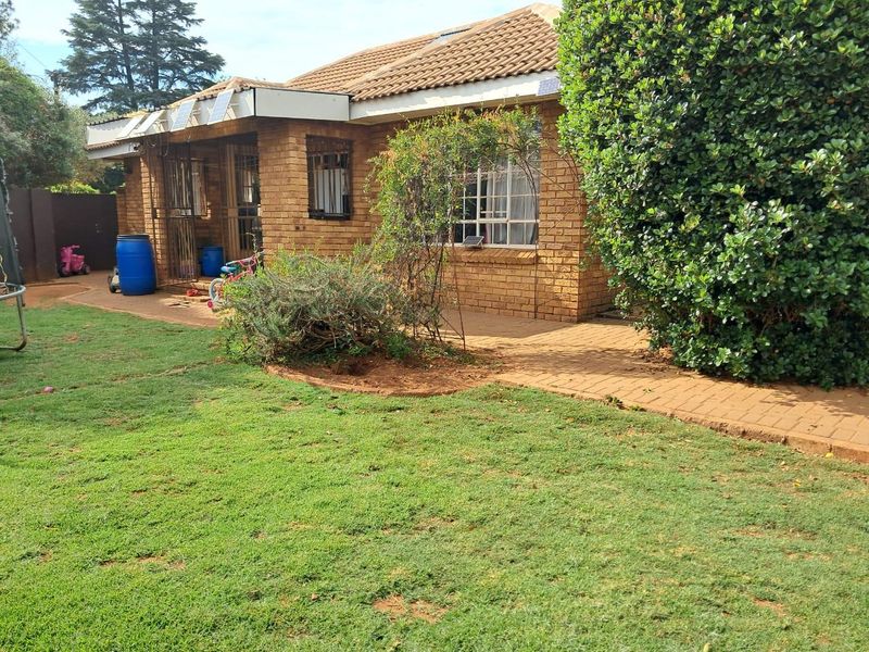 Rear view of a face brick house featuring a paved patio area, tiled roof, and solar panels, set within a private garden.