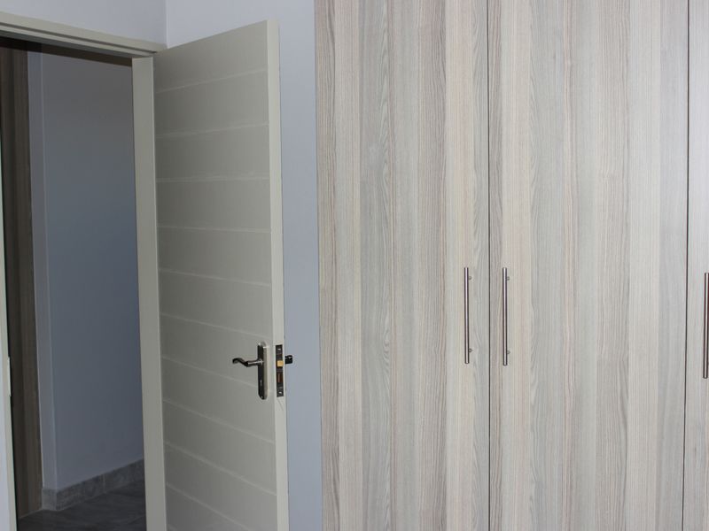 A clean bedroom interior featuring modern wood-grain built-in cupboards and a neutral door leading to an adjacent space.