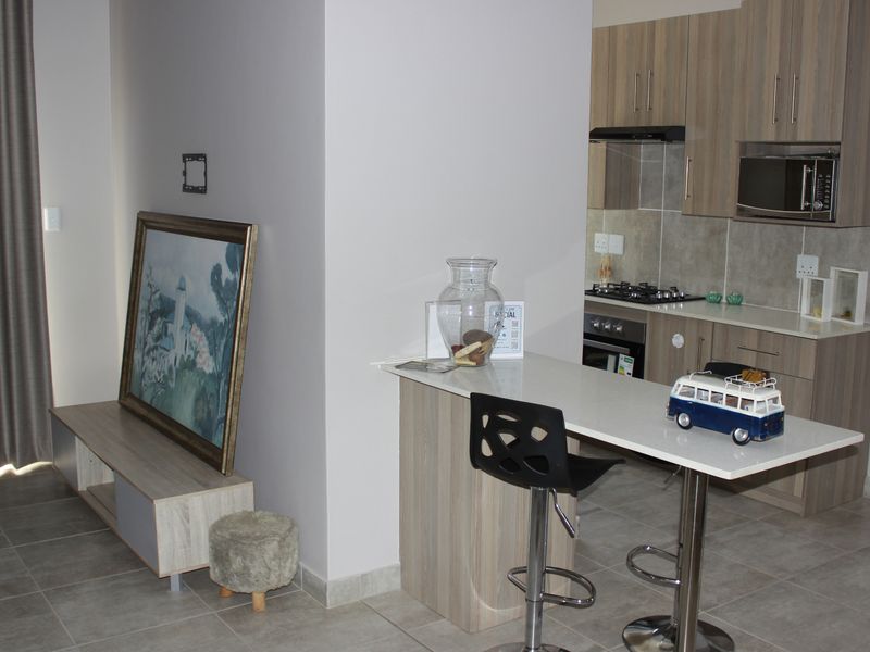 Open-plan living area featuring a modern kitchen with built-in cabinetry, stone countertops, gas hob, and a breakfast bar island.