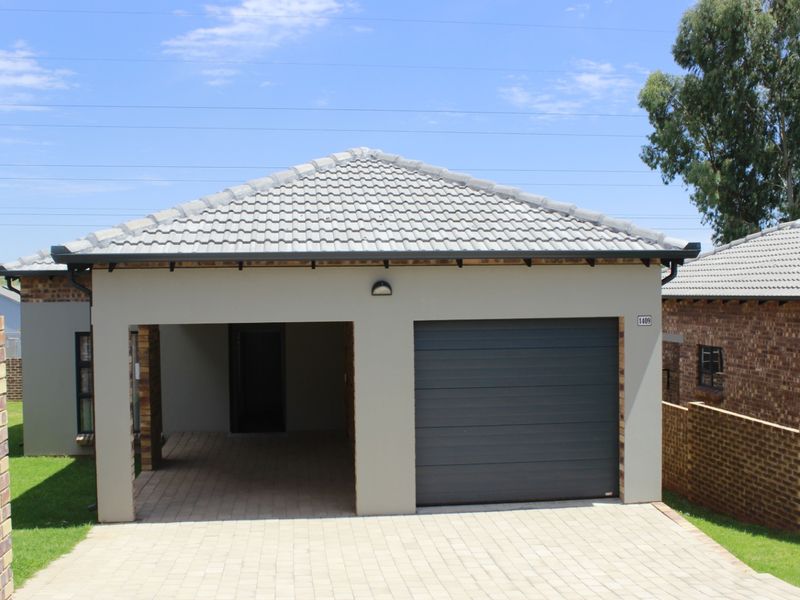 Front elevation of a modern house featuring a tiled roof, a single sectional garage door, and a paved driveway with brick boundary walls.