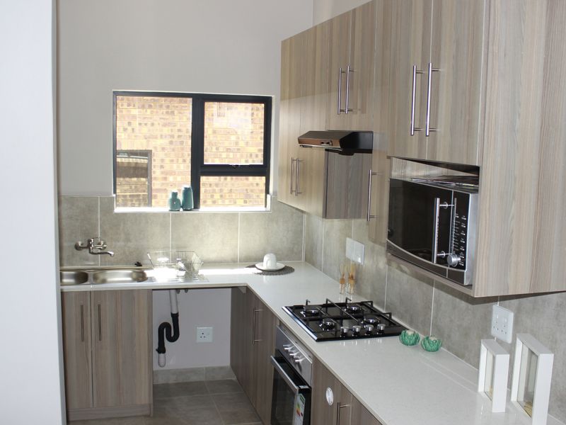 Modern kitchen featuring light wood-grain cabinetry, stone countertops, a gas hob, built-in oven, and integrated microwave with a neutral tiled backsplash.