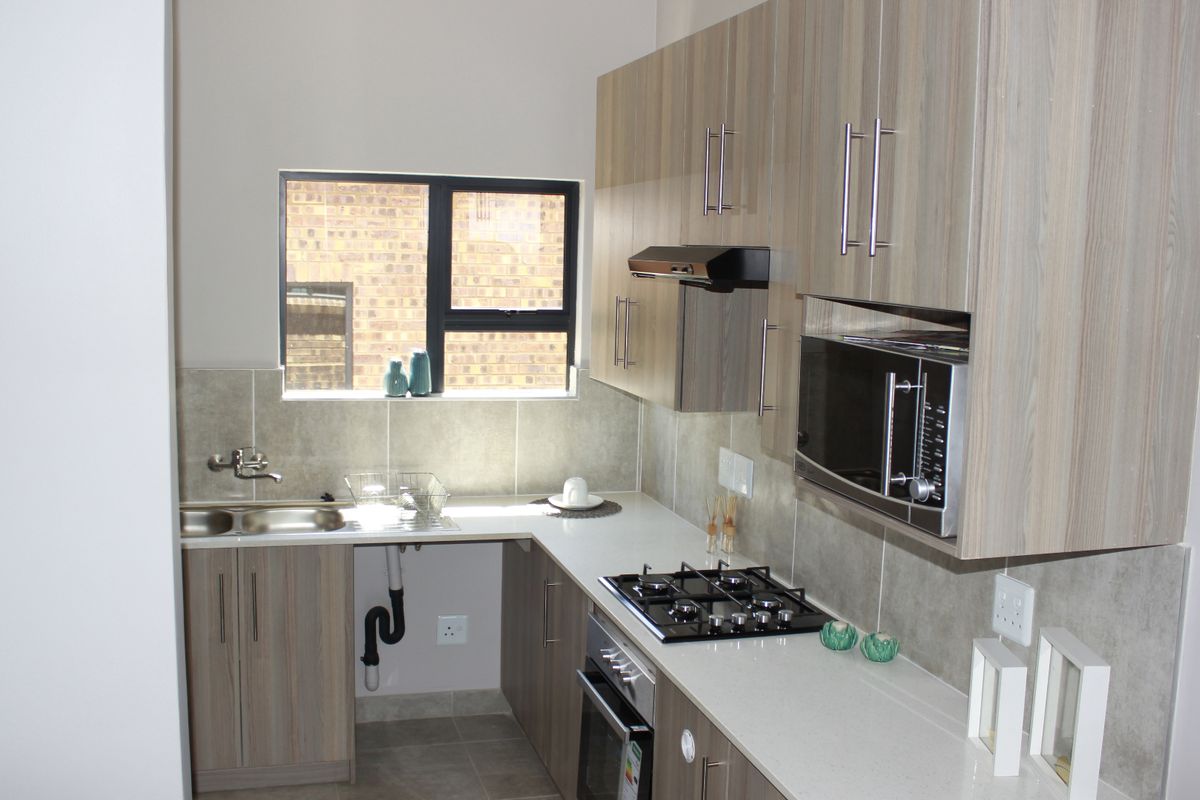 Modern kitchen featuring light wood-grain cabinetry, stone countertops, a gas hob, built-in oven, and integrated microwave with a neutral tiled backsplash.