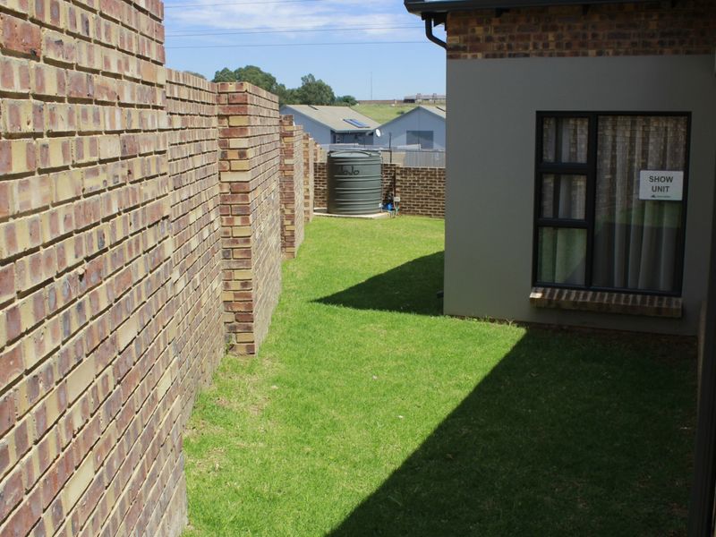 A side garden area featuring a face brick boundary wall, a water tank, and a modern plastered exterior wall with aluminium window frames.