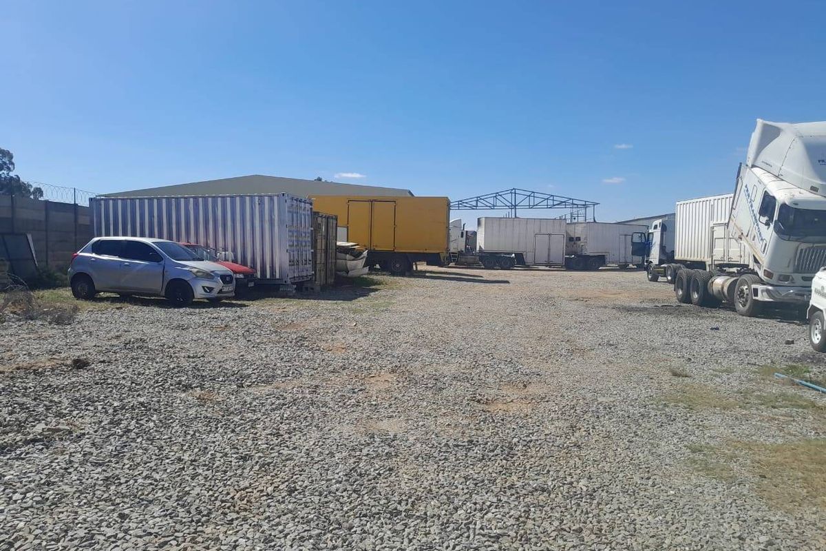 Commercial yard space featuring a large gravel-surfaced area, perimeter fencing, and industrial storage structures.