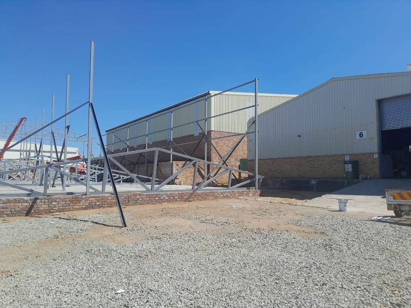 Exterior view of a commercial property undergoing construction, featuring an exposed steel framework and brick foundation on a gravel site.