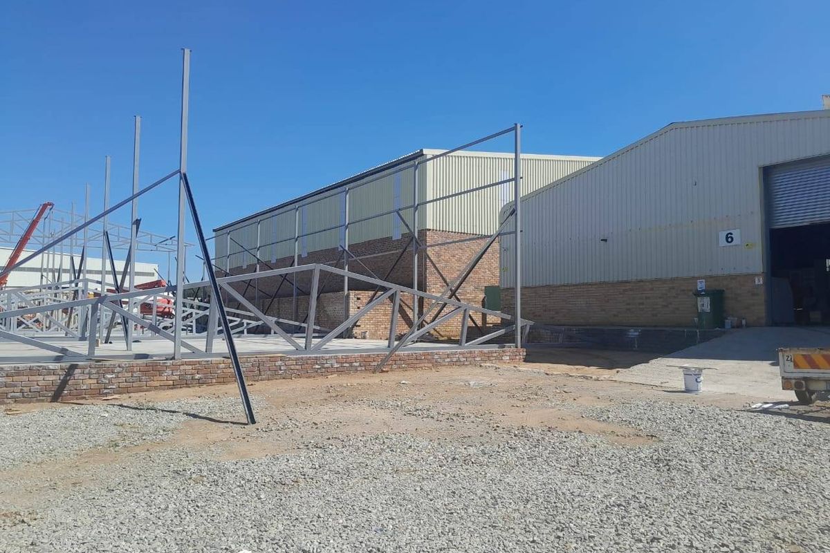 Exterior view of a commercial property undergoing construction, featuring an exposed steel framework and brick foundation on a gravel site.