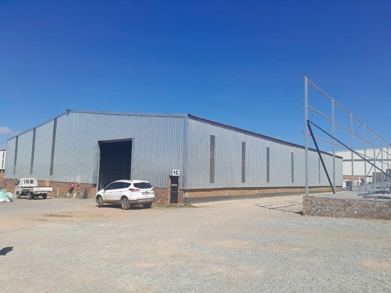 Commercial warehouse facility featuring corrugated metal cladding, large roller shutter access, and an adjacent unfinished steel structural frame.