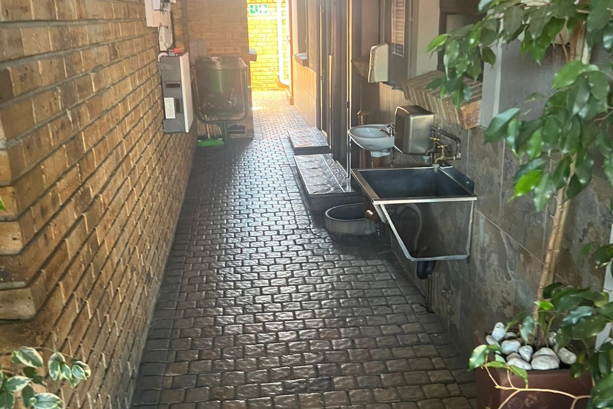 A narrow exterior side passage featuring paved flooring, a wall-mounted utility sink, and external air conditioning units.