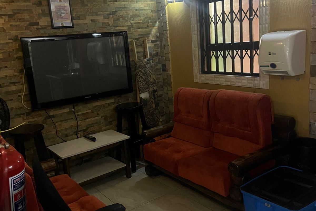 A compact living room featuring stone-cladding accent walls, tiled flooring, a wall-mounted air conditioning unit, and security bars on the window.