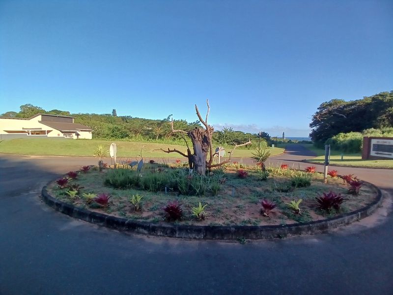 A view of the landscaped roundabout at the entrance of the residential estate, featuring established garden beds and paved access roads.
