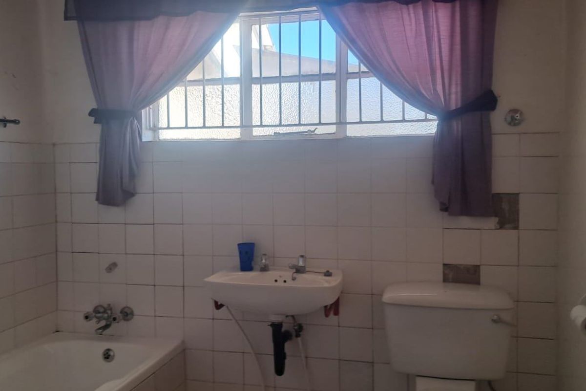 A dated bathroom featuring a bathtub, wall-mounted basin, and toilet, with visible missing wall tiles requiring maintenance or renovation.