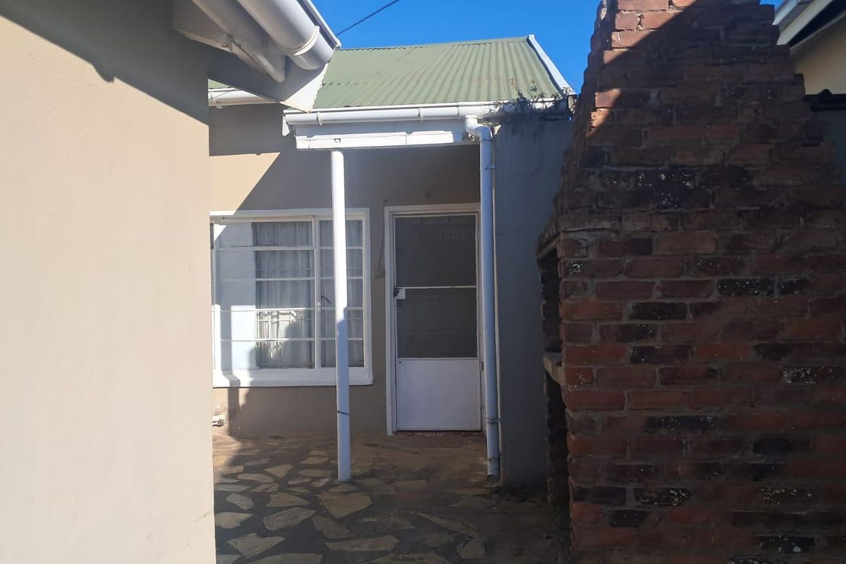 Rear exterior area featuring a brick braai, stone paved patio, and access to the main dwelling via a security screen door.