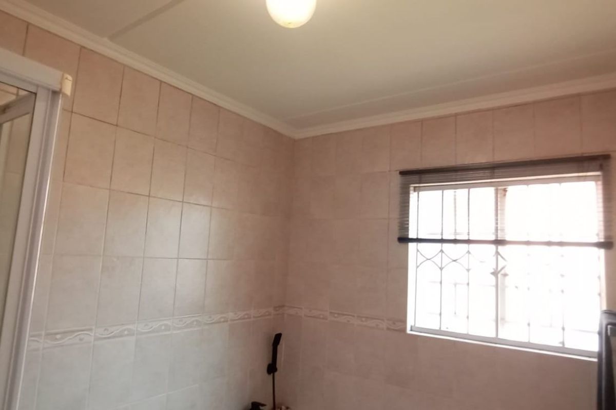 A functional bathroom featuring tiled walls, a shower enclosure, and a window with security bars.