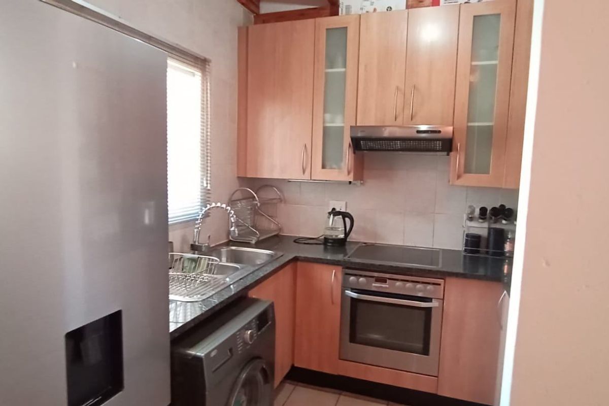 Compact kitchen featuring light wood cabinetry, dark countertops, integrated oven, electric hob, extractor fan, and a tiled backsplash.