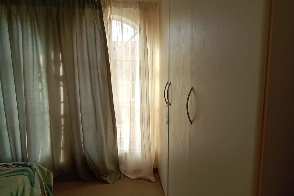 A bedroom featuring a built-in wardrobe and an arched window with curtains, providing natural light to the space.