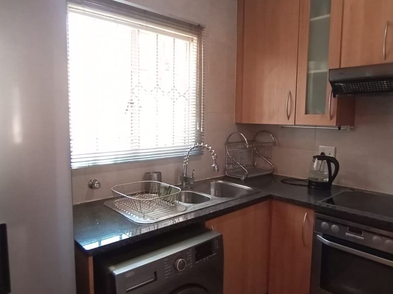 Functional kitchen featuring wooden cabinetry, granite countertops, integrated oven and hob, and a double sink with a window view.