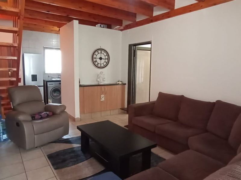 Open-plan living area featuring exposed timber ceiling beams, a wooden staircase, and tiled flooring, creating a functional and connected living space.