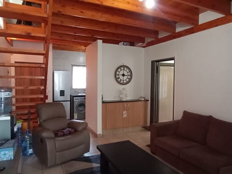 Open-plan living area featuring exposed timber ceiling beams, a wooden staircase, and tiled flooring, creating a warm and functional multi-purpose space.