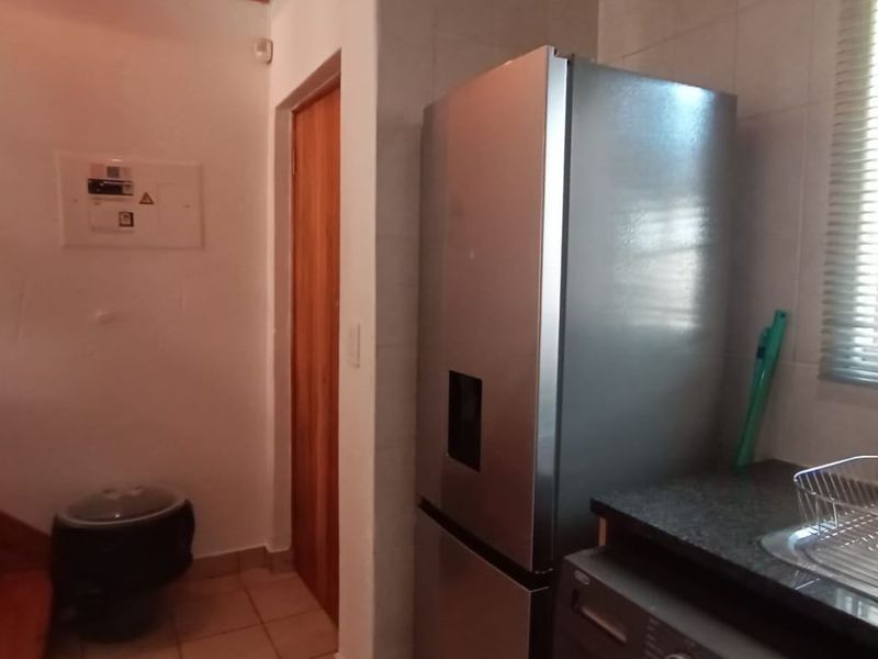 A functional kitchen area featuring a stone countertop, integrated sink, and tiled flooring, adjacent to a wooden staircase and electrical distribution board.