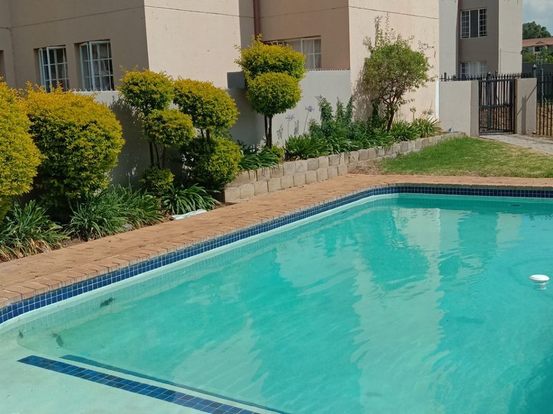 A well-maintained swimming pool area featuring brick coping, a retaining wall, and landscaped garden beds set against the apartment building exterior.