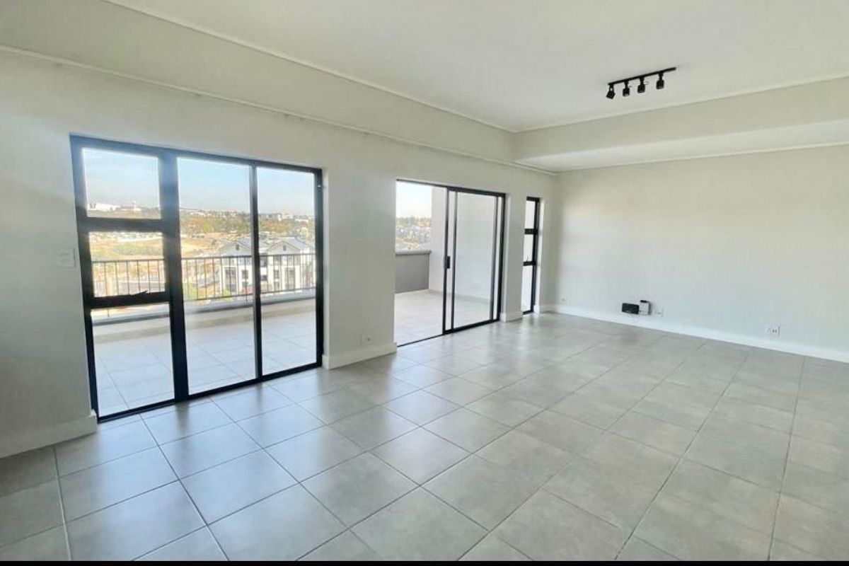 Spacious, light-filled living area featuring neutral tiled flooring, modern recessed lighting, and large sliding glass doors opening onto a private balcony.