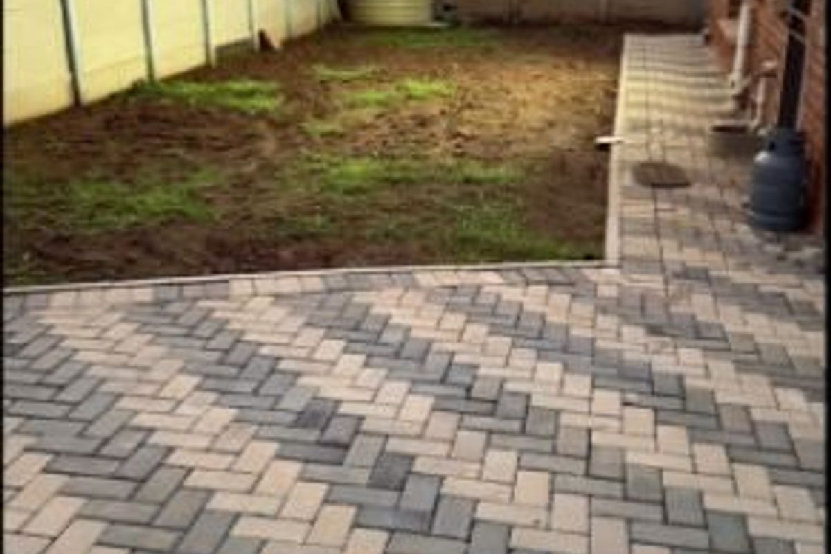 Rear garden area featuring a herringbone paved patio, perimeter precast concrete walling, and a water storage tank.