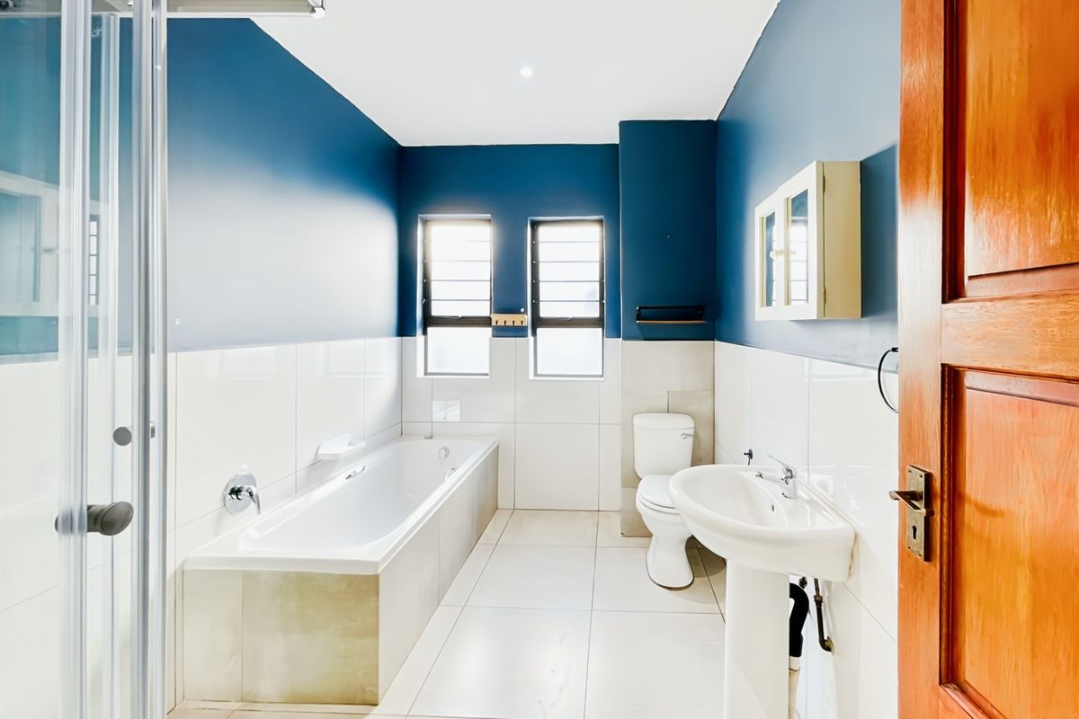 A bright, modern bathroom featuring a built-in bathtub, pedestal sink, toilet, and a glass-enclosed shower, finished with tiled walls and floors.