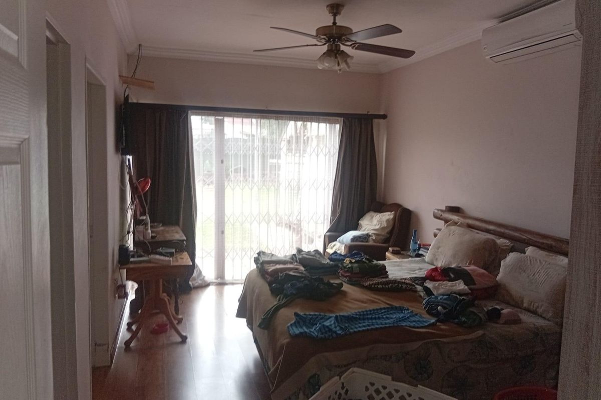 A bedroom featuring laminate flooring, a ceiling fan, and a wall-mounted air conditioning unit, with access to the exterior via a sliding glass door.