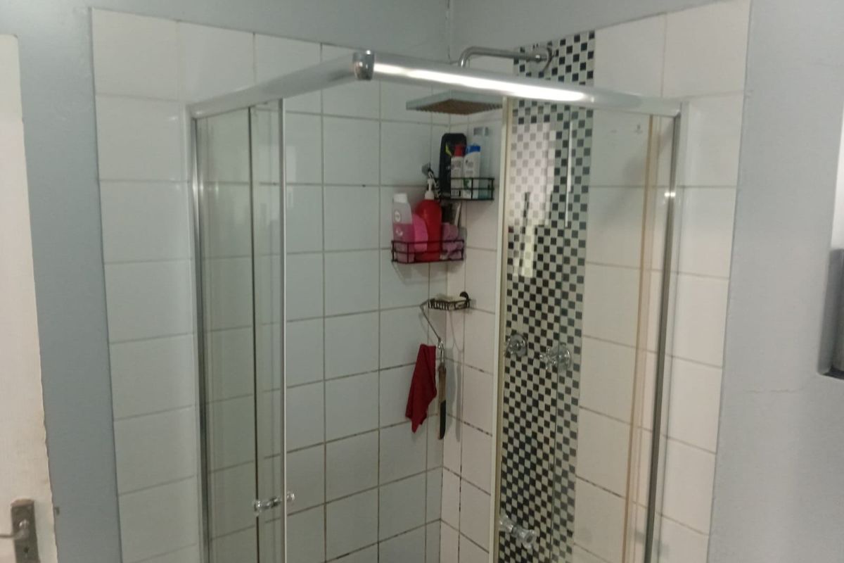 A bathroom shower enclosure featuring white wall tiles with a decorative black and white checkered accent strip.