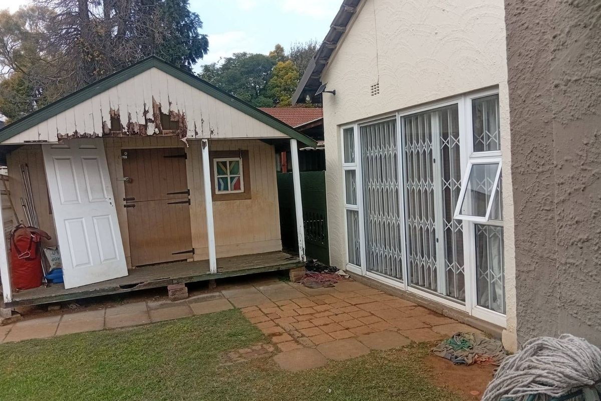 Rear exterior view showing a paved patio area, sliding glass doors with security gates, and a detached timber garden shed requiring maintenance.