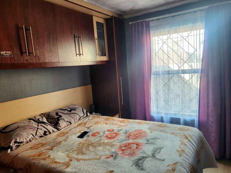 Bedroom featuring built-in wooden cupboards and security bars on the window. The ceiling shows signs of water damage and requires maintenance.