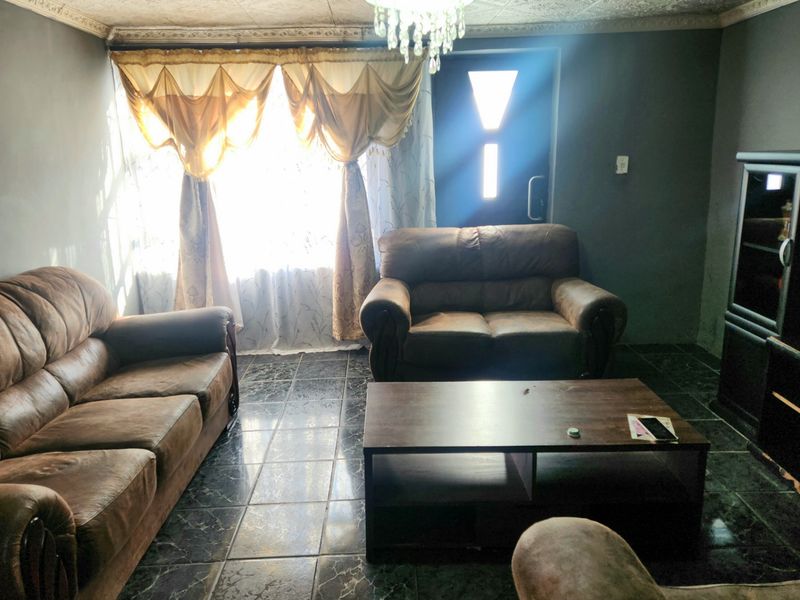 A living room featuring dark tiled flooring, a decorative ceiling with coving, and natural light entering through the front entrance.