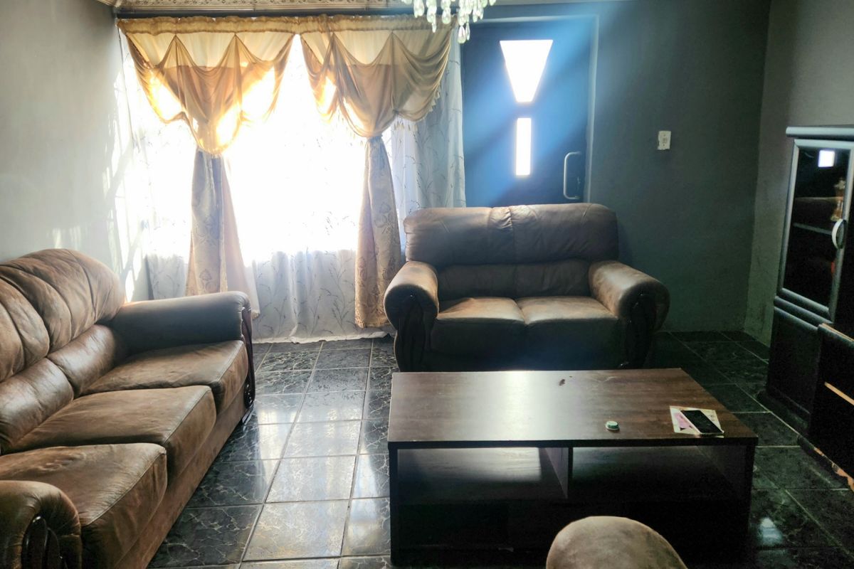 A living room featuring dark tiled flooring, a decorative ceiling with coving, and natural light entering through the front entrance.
