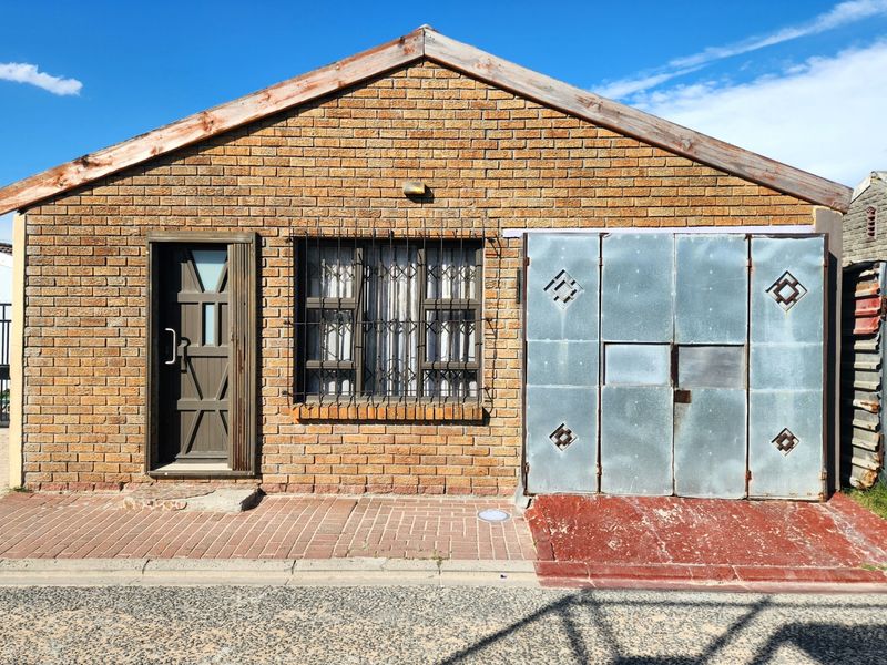 Front elevation of a face brick house featuring a security-gated entrance, window security bars, and a metal garage door with a paved driveway.