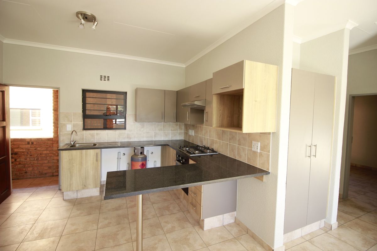 A functional kitchen featuring granite countertops, a gas hob, extractor fan, and ample built-in cabinetry, with tiled flooring throughout.