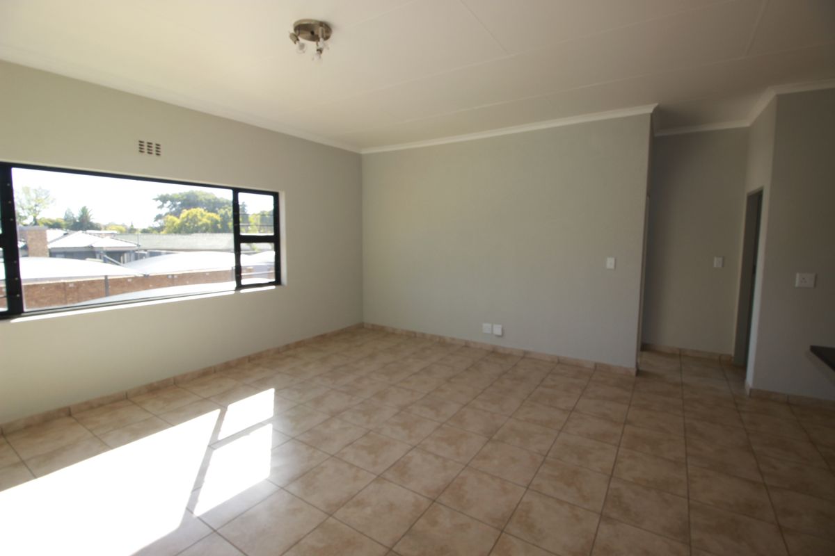 A bright, empty living area featuring neutral wall paint, tiled flooring, and a large window providing natural light.