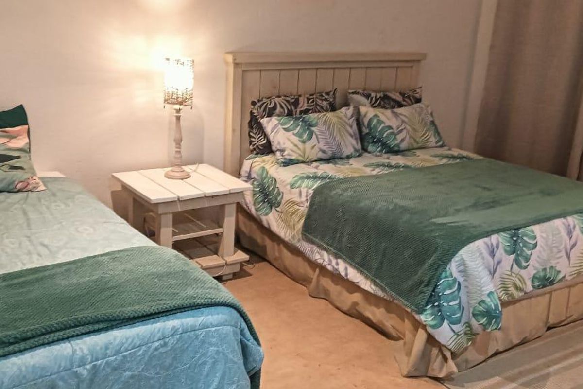 A bedroom featuring a double bed and a single bed, with neutral wall finishes and floor-to-ceiling curtains.