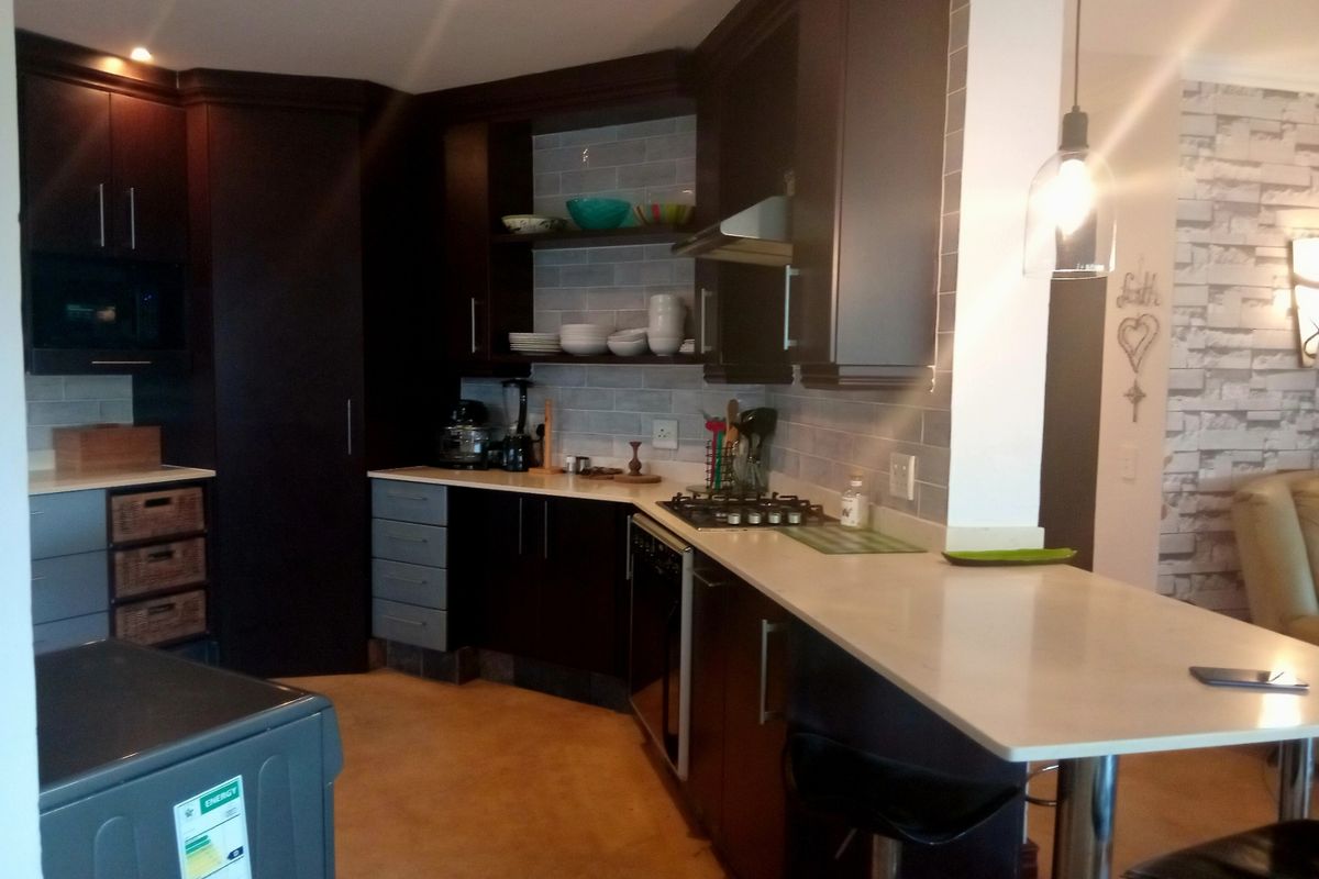 Modern kitchen featuring dark cabinetry, stone countertops, a breakfast bar, and a gas hob with an integrated extractor fan.