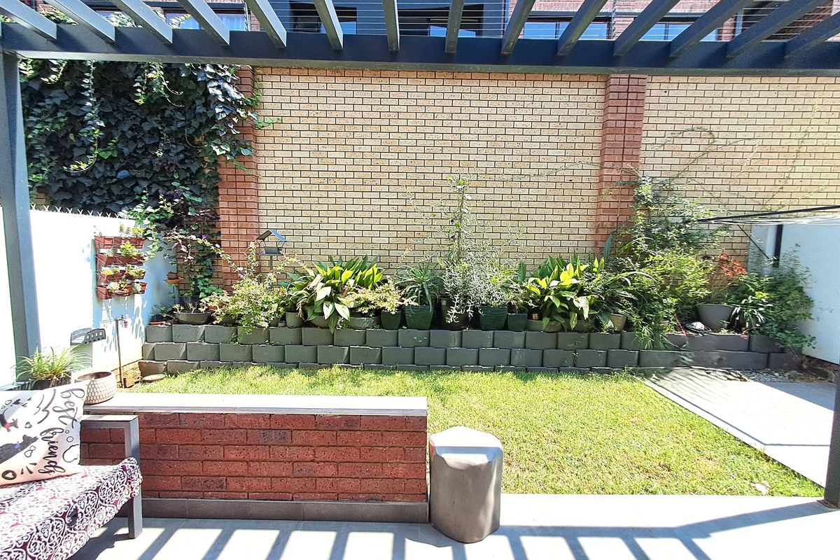 A private rear garden featuring a paved patio area with a timber pergola, a brick retaining wall, and established garden beds.