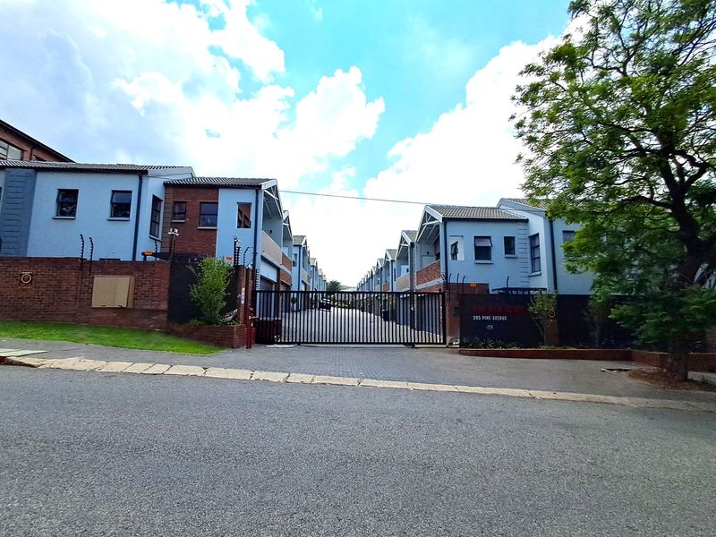 Street view of the townhouse complex entrance, featuring a secure gated access point, paved driveway, and modern multi-level residential units.